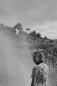 Woman standing by splashing water against sky