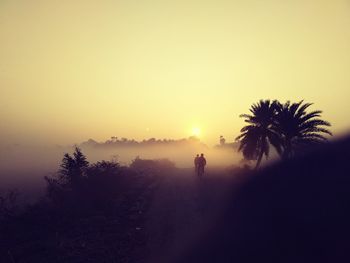 Silhouette boys on road against clear orange sky