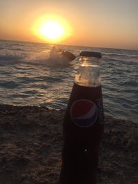 Close-up of beer bottle against sea during sunset