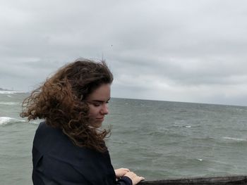 Young woman standing at beach against sky