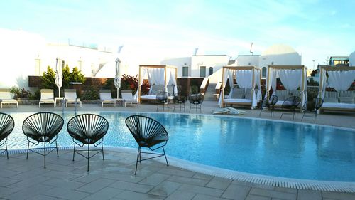 Chairs by swimming pool against sky