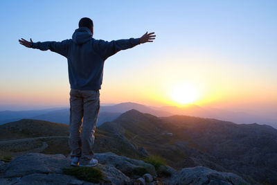 Male stands towards the sun on mountain slope with spread arms. man meets the dawn with open arms