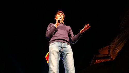 Man speaking on microphone while standing against sky at night