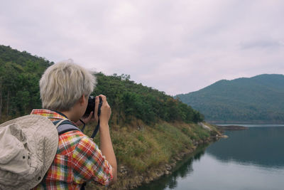 Man photographing by lake against sky