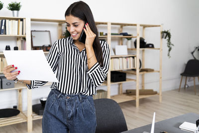 Young woman using phone while sitting on table