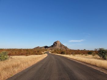 Road amidst land against clear blue sky