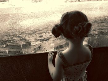 Rear view of girl standing by window