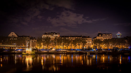 Illuminated buildings in city by river at night