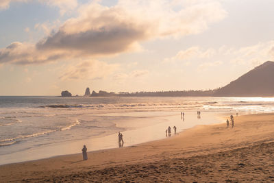 People at beach against sky during sunset