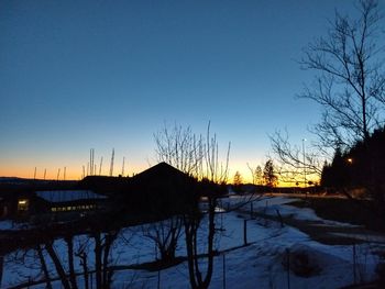 Silhouette trees by lake against clear sky during sunset