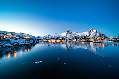 Scenic view of lake by snowcapped mountains against blue sky