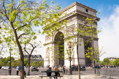 Low angle view of arc de triomphe by road against blue sky