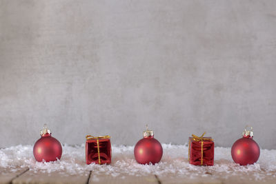 Red christmas presents and baubles on table against wall