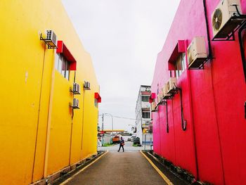 Rear view of man walking on alley amidst buildings in city