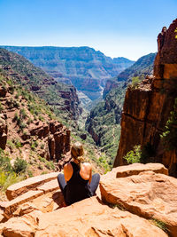 Rear view of young woman sitting on mountain on sunny day