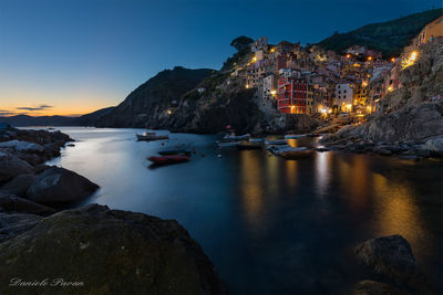 View of illuminated city at waterfront during sunset