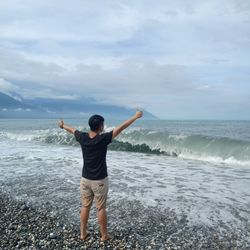 Rear view of man standing at beach against sky