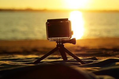 Close-up of camera on beach against sky during sunset