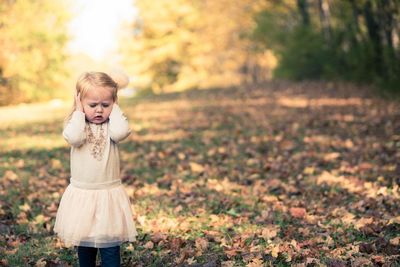 Girl covering ears with hands while standing on field during autumn