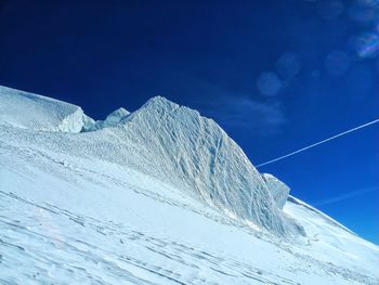 Low angle view of snowcapped mountains against blue sky on sunny day