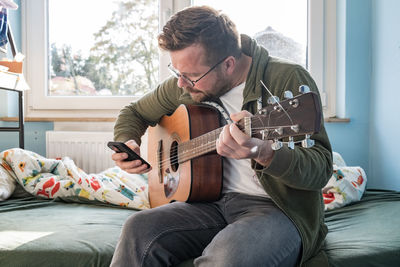 Man playing guitar while sitting on sofa at home