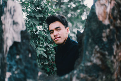 Portrait of young man against tree trunk in forest