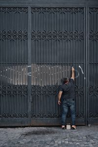 Rear view of man painting black gate