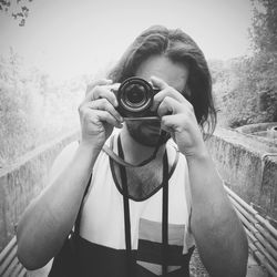 Young woman photographing while standing against white background