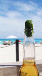 Close-up of beer bottle at beach against sky