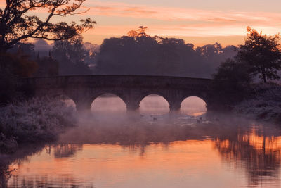 Arch bridge over river against sky during sunset