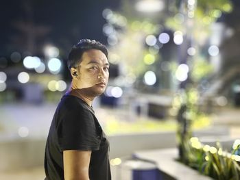 Portrait of young man standing against illuminated city at night