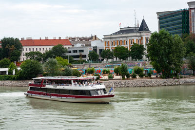 Boat sailing on river by buildings in city against sky