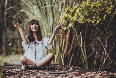 Full length of smiling woman playing with dry leaves on boardwalk