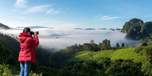 Woman photographing landscape against sky