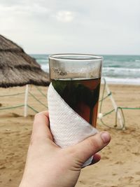 Midsection of man holding glass at beach against sky