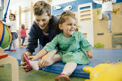 Pre-school teacher helping little girl putting a shoe on