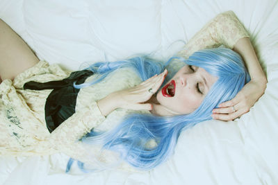 High angle view of woman with dyed hair yawning on bed