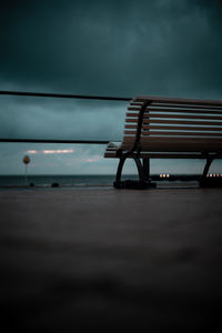 Empty bench on beach against sky at dusk
