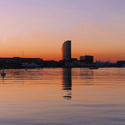 Buildings by river against sky during sunset