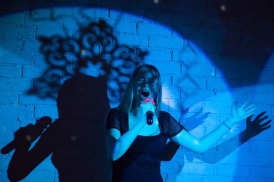 Teenage singer performing against shadow on brick wall