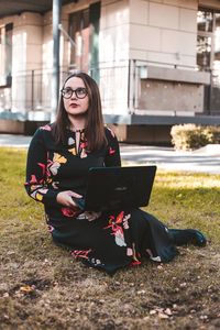 Thoughtful young woman using laptop while sitting on field