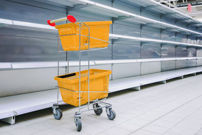 Shopping trolley against empty shelves in grocery store, shortage of goods, copy space