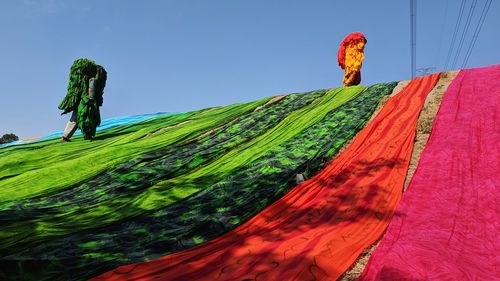 Low angle view of people carrying textile while walking on mountain against sky