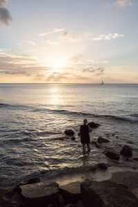 Rear view of woman standing sea against sky during sunset