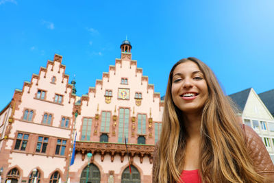 Portrait of smiling young woman against building against sky