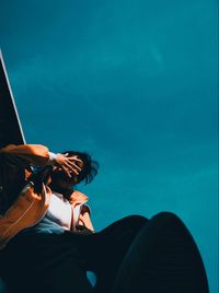 Low angle view of women sitting against blue sky