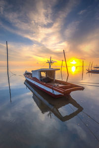 Boat moored in water against sky during sunset