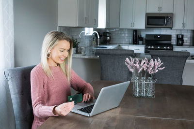 Young woman using phone while sitting on table at home