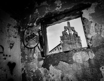 Low angle view of cross against sky seen through window