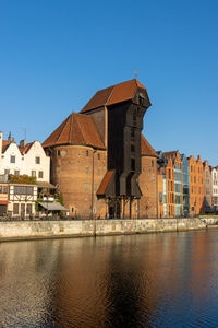 Buildings by river against clear blue sky